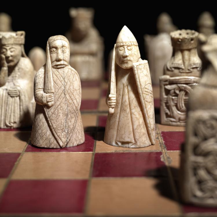 The Lewis Chessmen on a chessboard mid-game, three figures in focus with eyes wide.