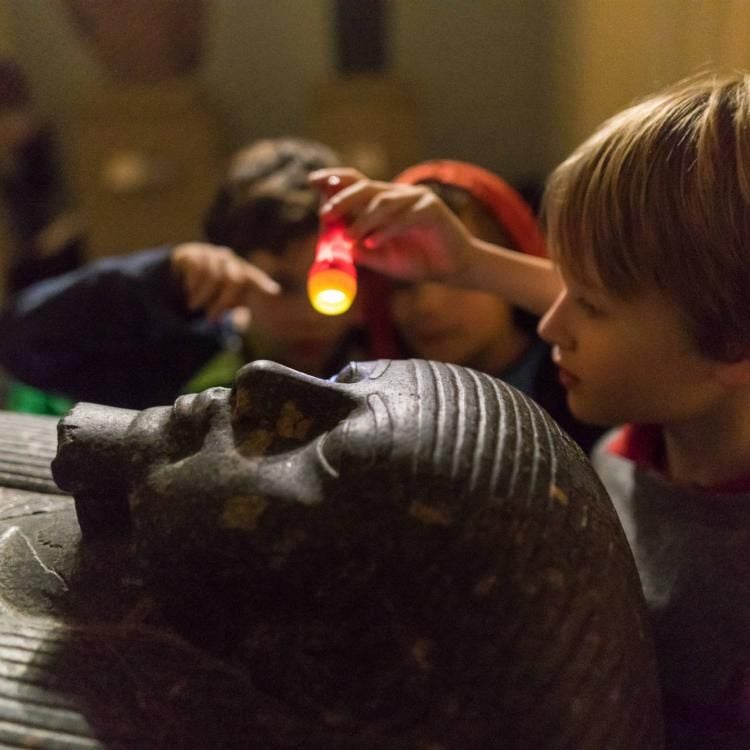 Children looking at an Egyptian sculpture by torchlight at a Museum sleepover.