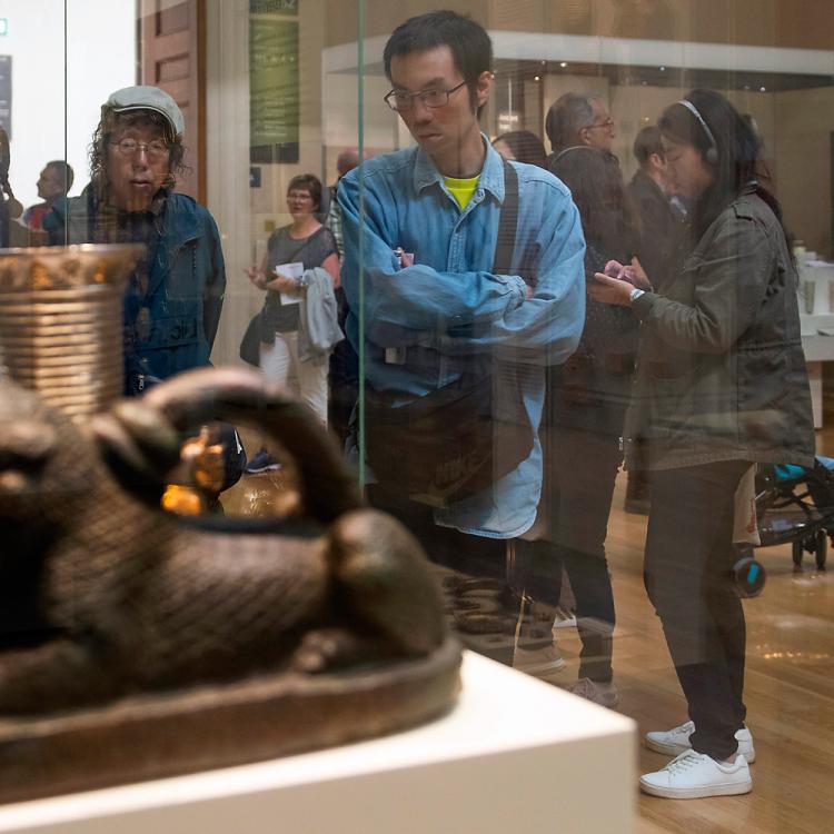 Visitors walk around Room 52. To the left are many objects in a display case. On the right, visitors walk around looking at objects
