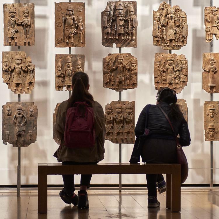 Two visitors viewing a wall of Benin plaques