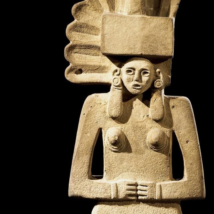 Female figure made of sandstone, standing with hands folded in front and with a fan-shaped headdress.