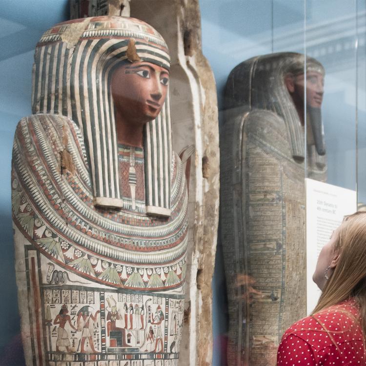 Two visitors looking up at mummies standing in a case.