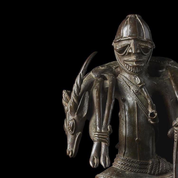 Bronze figure of a man wearing a helmet, carrying an antelope around his shoulders. 