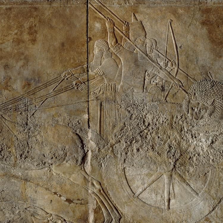 Stone relief depicting the king driving a spear into a wounded lion that is biting the wheel of the chariot