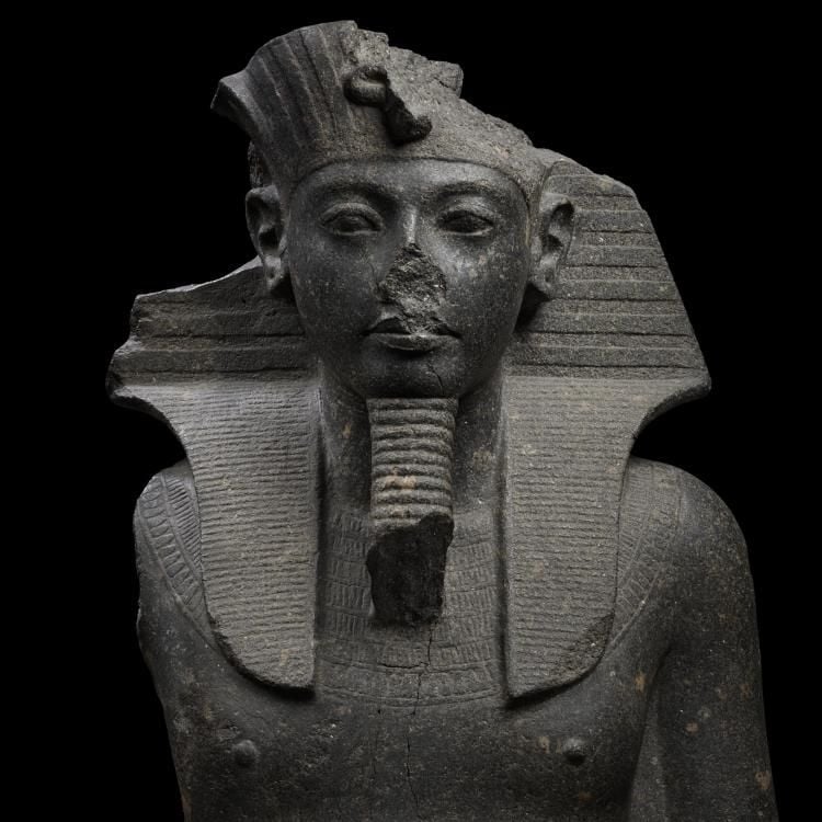 Upper section of a granite statue of Tutankhamun, wearing a headcloth, false beard, beaded broad collar.