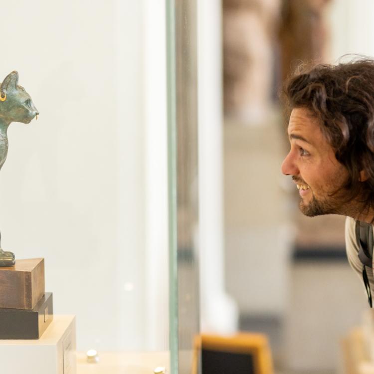 Two Members closely inspecting Gayer-Anderson cat, a bronze figure depicting one form of the goddess Bastet. 
