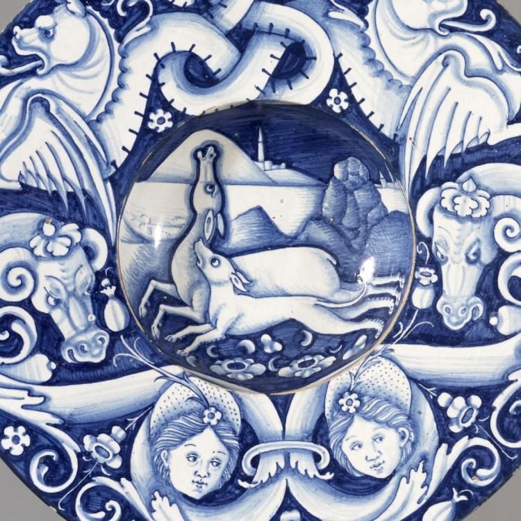Broad-rimmed bowl or plate with well in shades of blue depicting deer being attacked by a dog in the centre, on rim intertwining monsters, heads and flowers