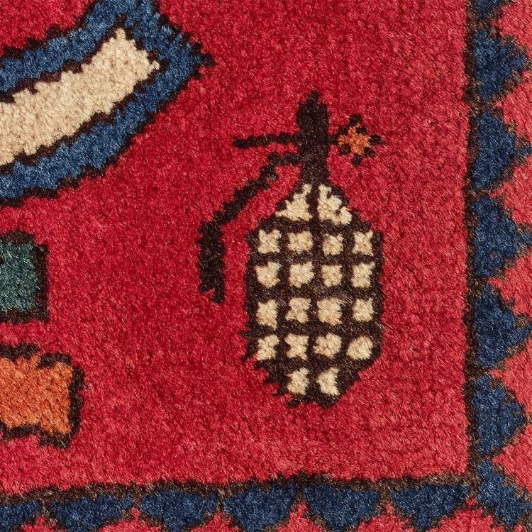 Detail of an Afghan war rug, showing a hand grenade and part of an assault rifle on a red background.