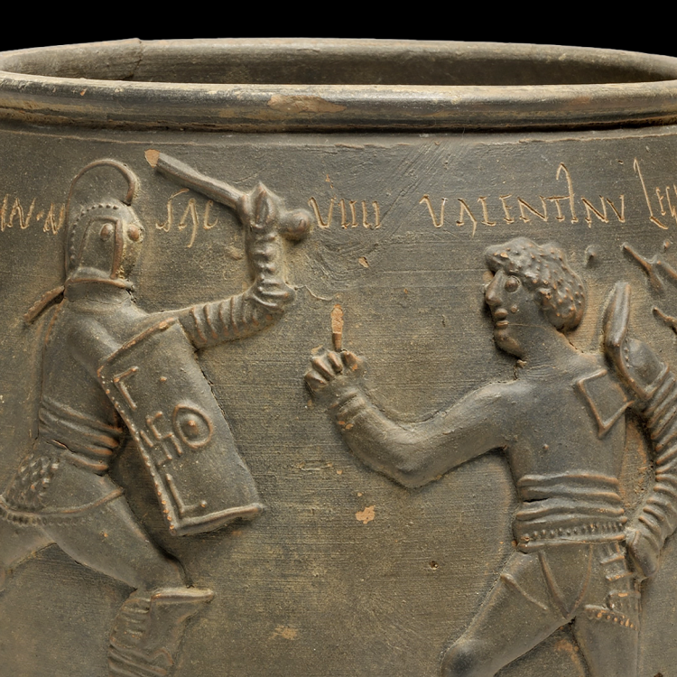A ceramic vase depicting a gladiator fight, in which a lesser armed gladiator raises a finger to signal defeat as a heavily armed gladiator attacks