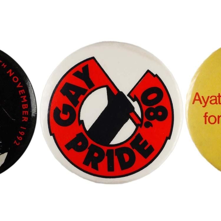 A black badge with Freddie Mercury in a colourful waistcoat on it and a red AIDS ribbon, next to a badge that has a large red banner with the words GAY PRIDE '08. Two other badges are visible, one with red text on white background and another with red text on a yellow background.