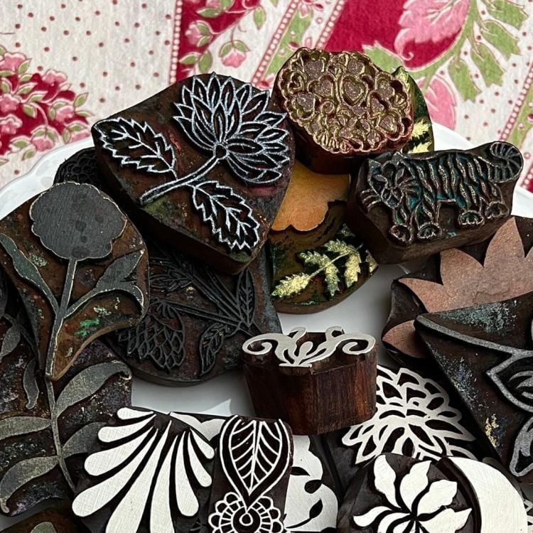 View of a plate full of individual woodblock prints ranging from floral to animal designs, held over a brightly patterned fabric.