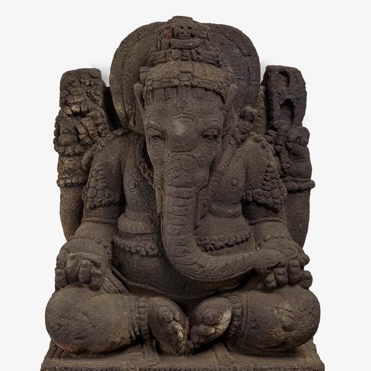 A dark stone carving of the elephant-headed god Ganesha seated cross-legged on a throne.