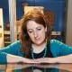Naomi Speakman rests her arms on a glass display case and wears a teal cardigan and turquoise beaded necklace