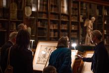 Patrons viewing framed drawings under lamplight in the Enlightenment gallery.