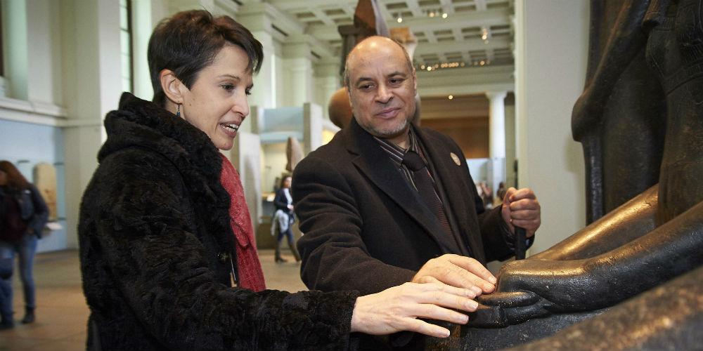 Two people touching Egyptian sculpture