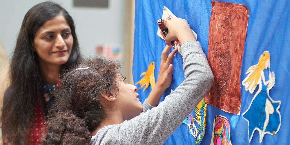 Woman watching child adding picture to a wall of art