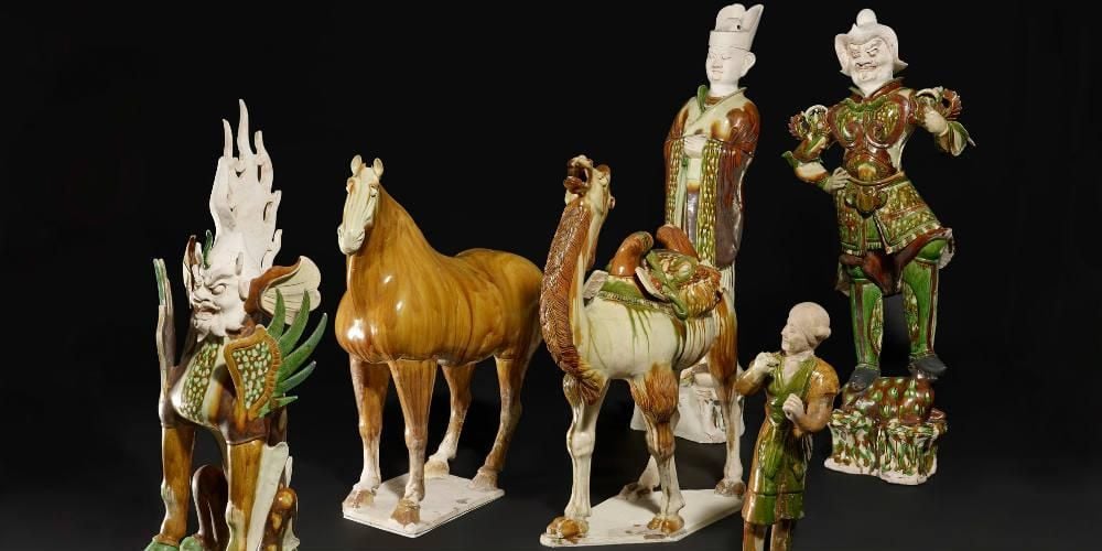 Four humans, one horse, one camel – all figures are shades of white, brown and green. They are Chinese tomb figures said to have come from the tomb of a general who died in AD728 during the Tang Dynasty. 