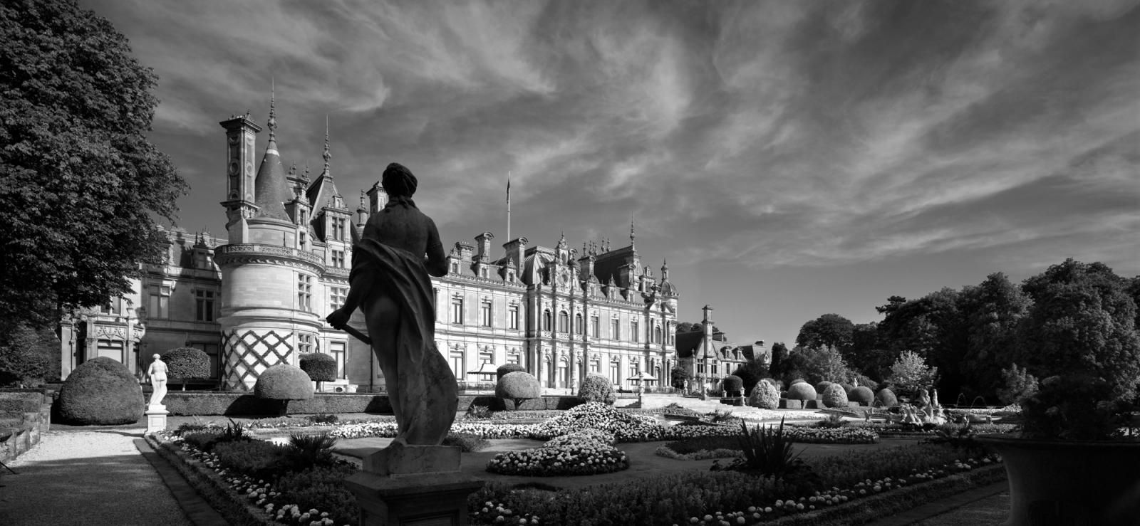 Black and white image of a large manor from outside with beautiful gardens.