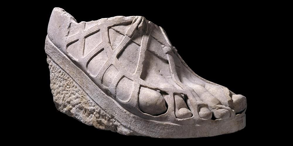 Colossal marble sculpture of a right foot wearing an elaborate Greek sandal.