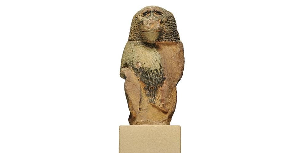 Glazed limestone statuette of a baboon, left side and arm missing and abrasions on face and head.