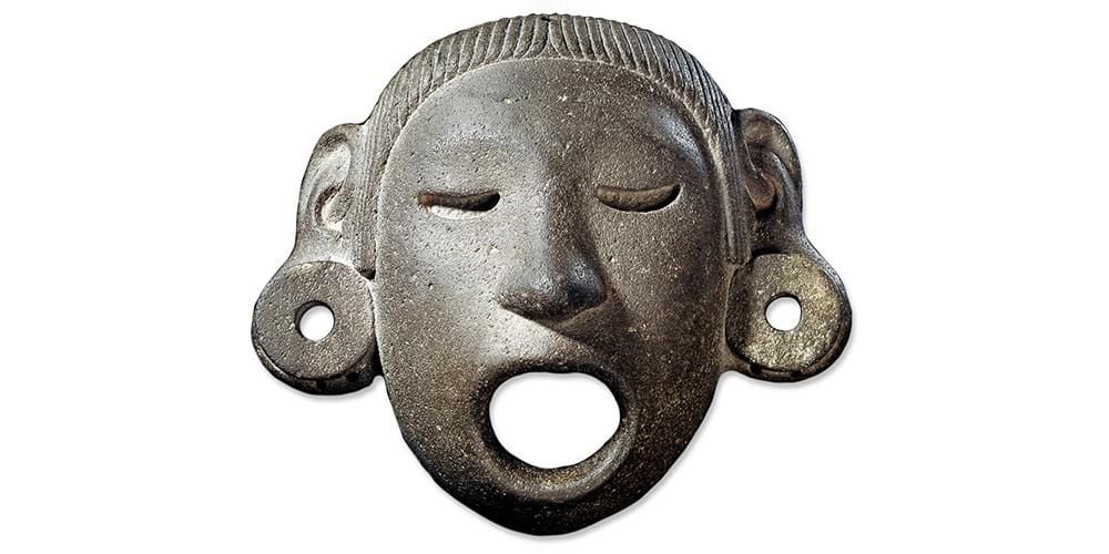 Stone human face-shaped mask of Xipe Totec represented wearing a flayed human skin, with earplugs.