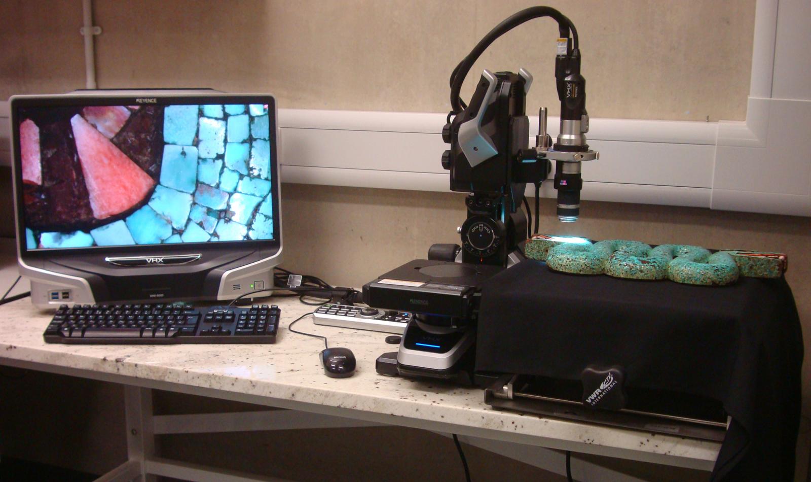 On the right, a turquoise double-headed serpent mosaic is under a scientific camera lens and the images displayed on a monitor on the left.