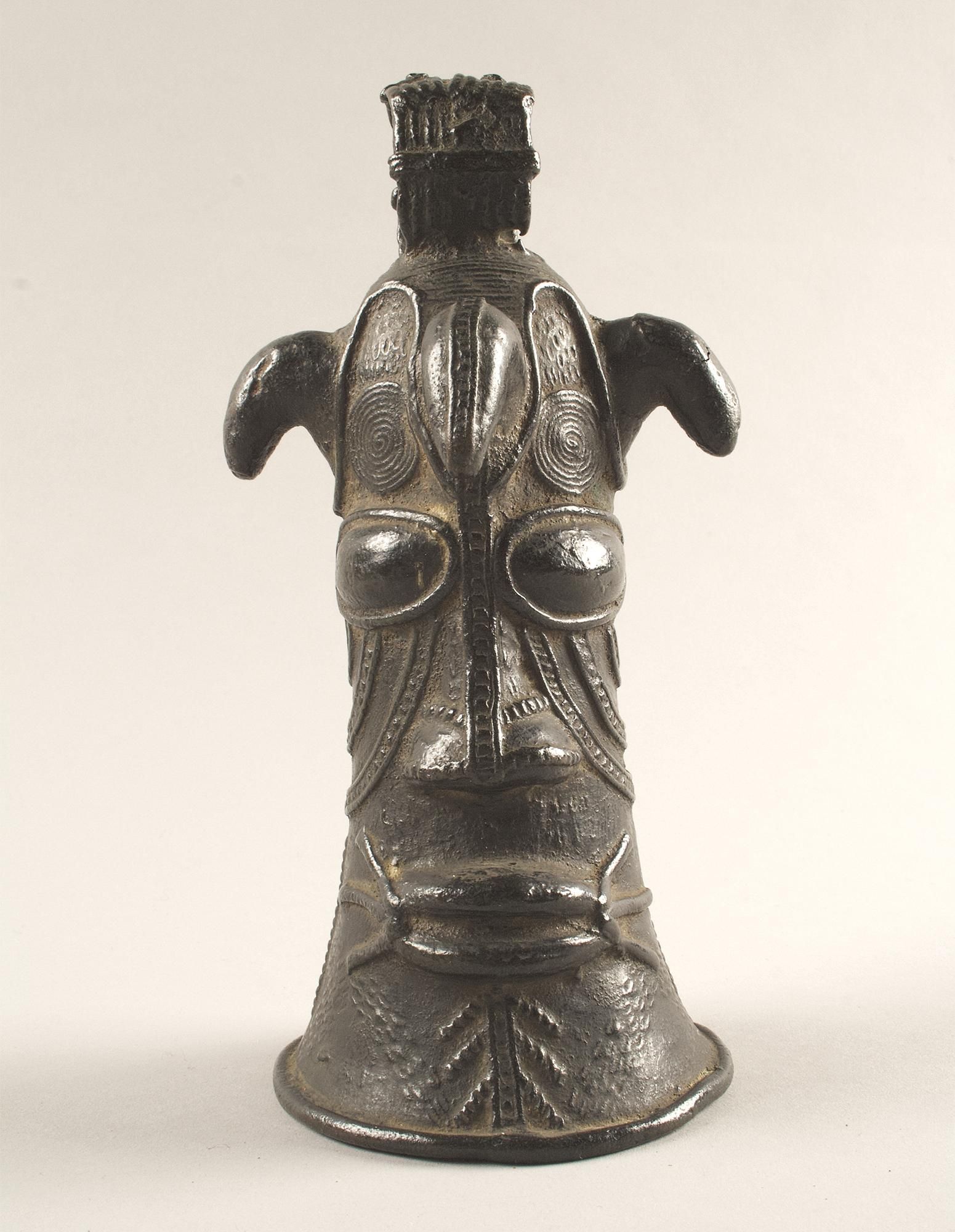 Horned bell head in a conical form depicting a face, with lined decoration across the cheeks and forehead.