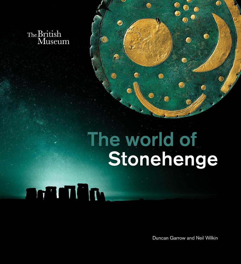 The front cover of The world of Stonehenge exhibition publication, featuring a photo of Stonehenge at night with a blue hue on the horizon below the night sky. In the top-right corner is the Nebra Sky Disc, a green round disc with yellow circles and crescent shapes believed to represent the night sky.