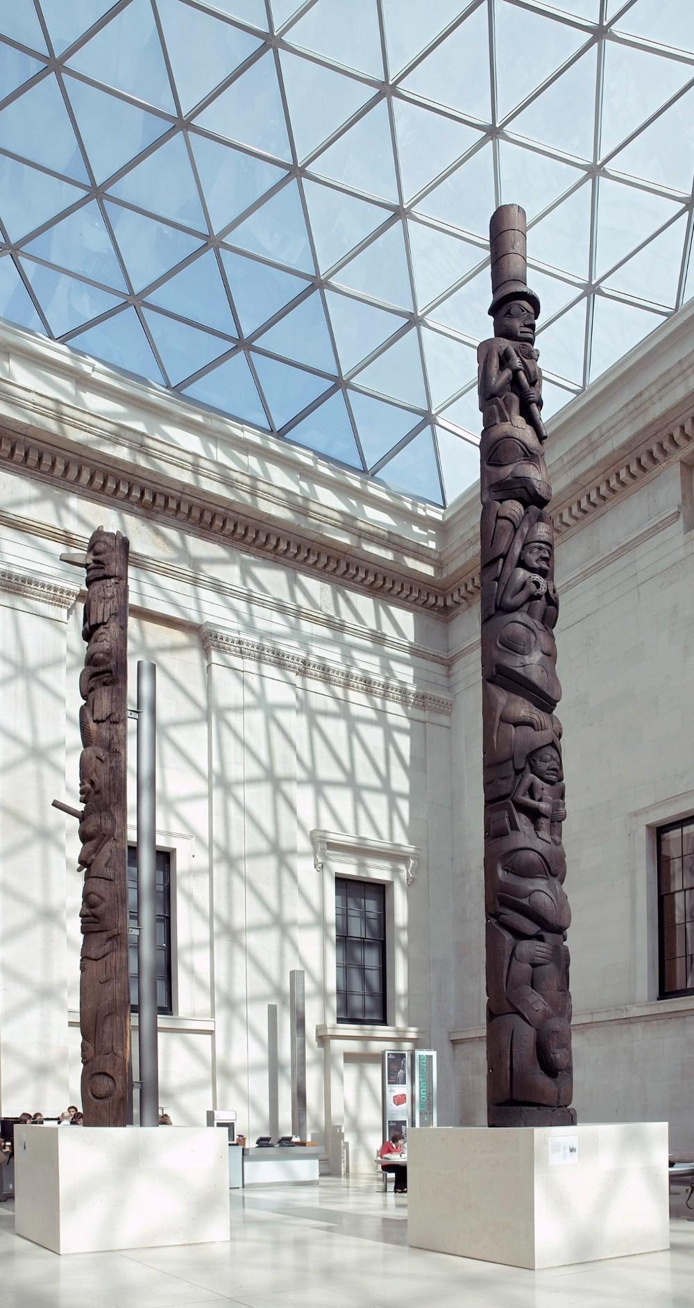 Carved cedar wood totem pole reaching up towards the glass ceiling of the Great Court