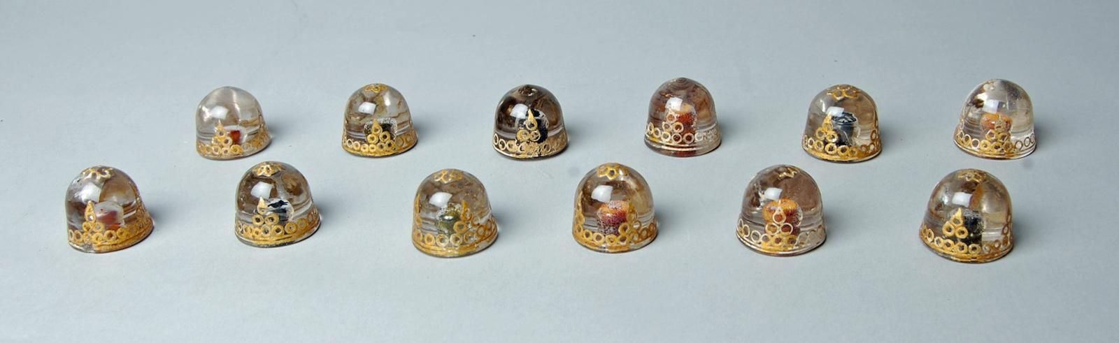 12 dome-shaped game pieces made of crystal, yellow painted pattern on top