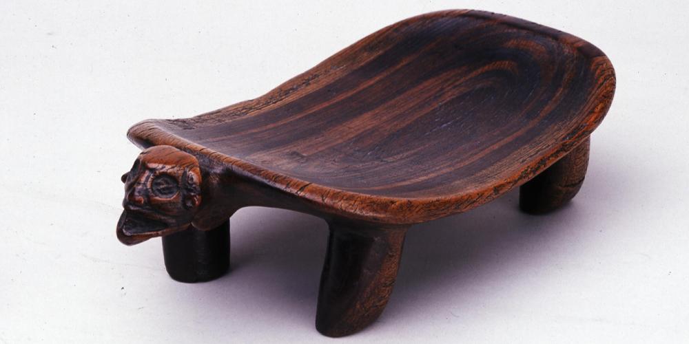 A rectangle-shaped concave wooden stool, with a face at the front opened mouthed. 