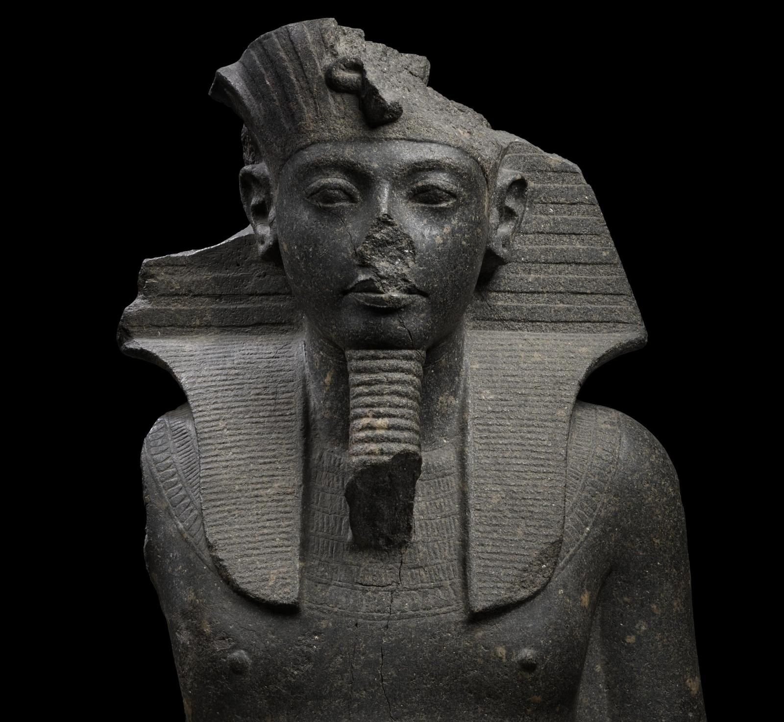 Upper section of a granite statue of Tutankhamun, wearing a headcloth, false beard, beaded broad collar.