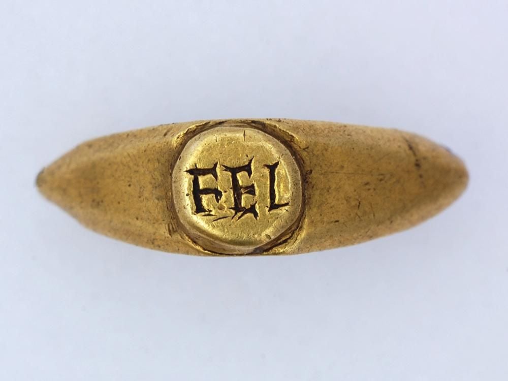 Dull gold tapered ring featuring a roughly formed bezel inscribed with what appears to read "FEL" - there are several deep scratches around the edges of each character while the band of the ring shows minor wear.