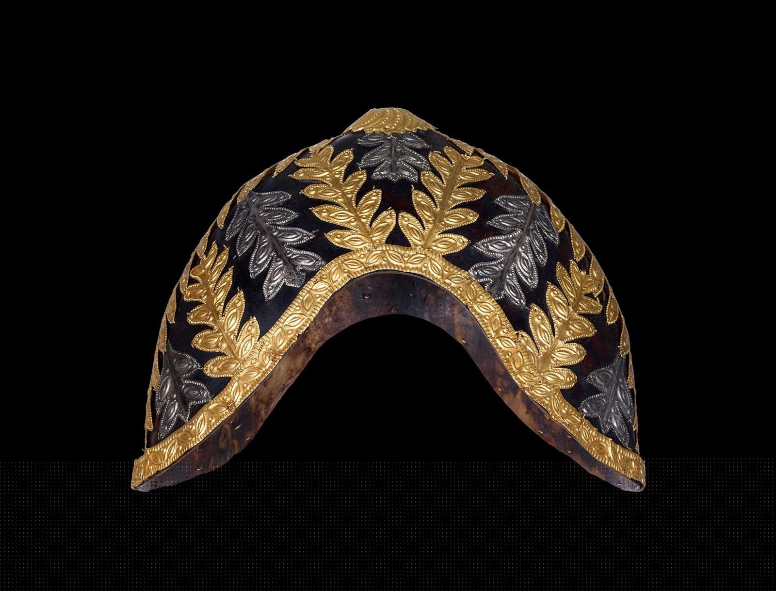 Kidney-shaped cap made of blackened animal hide, covered in strips of gold and silver in the shape of leaves
