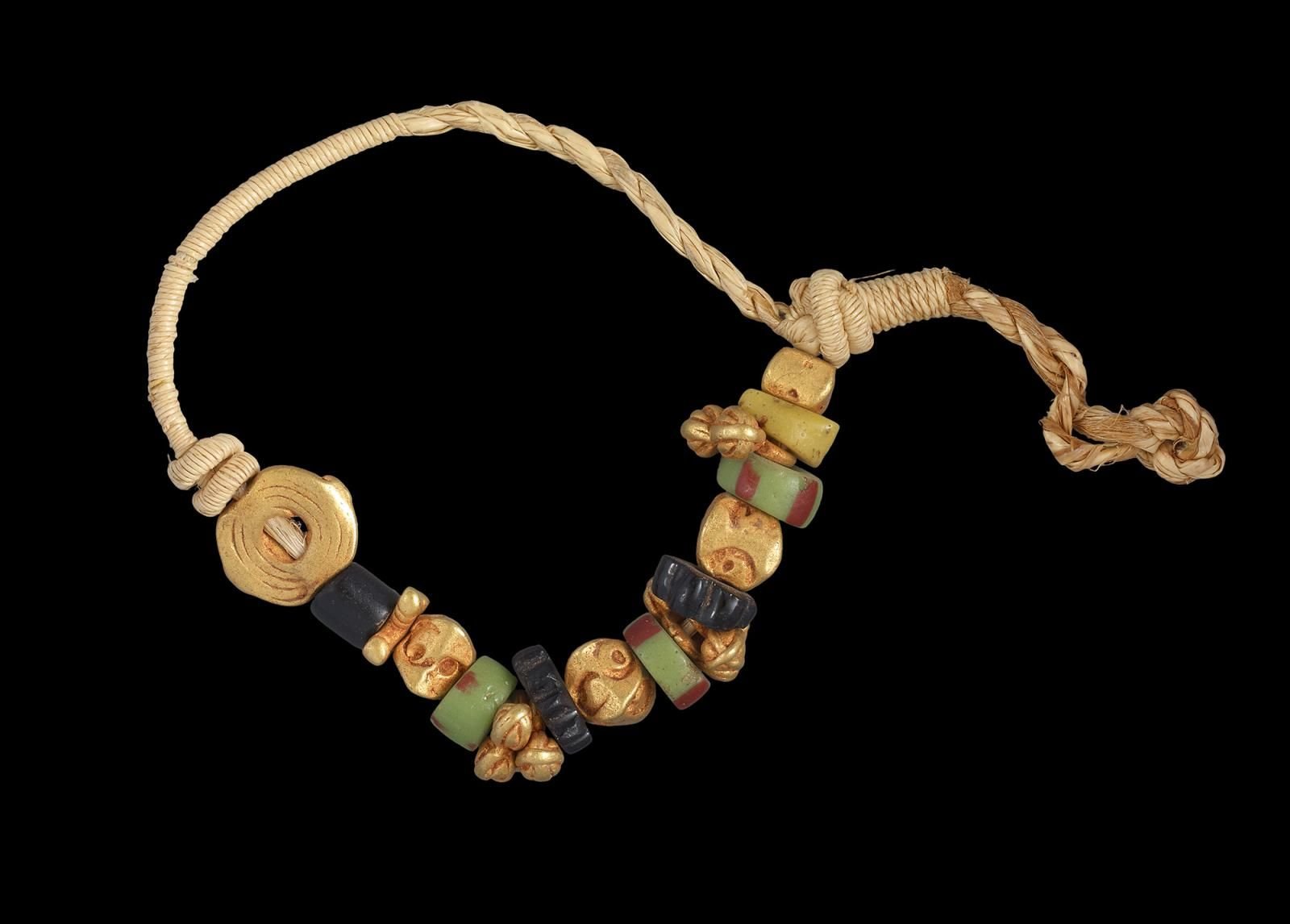 Bracelet with beads made of gold and green and black glass, on a cord of tightly coiled fibre