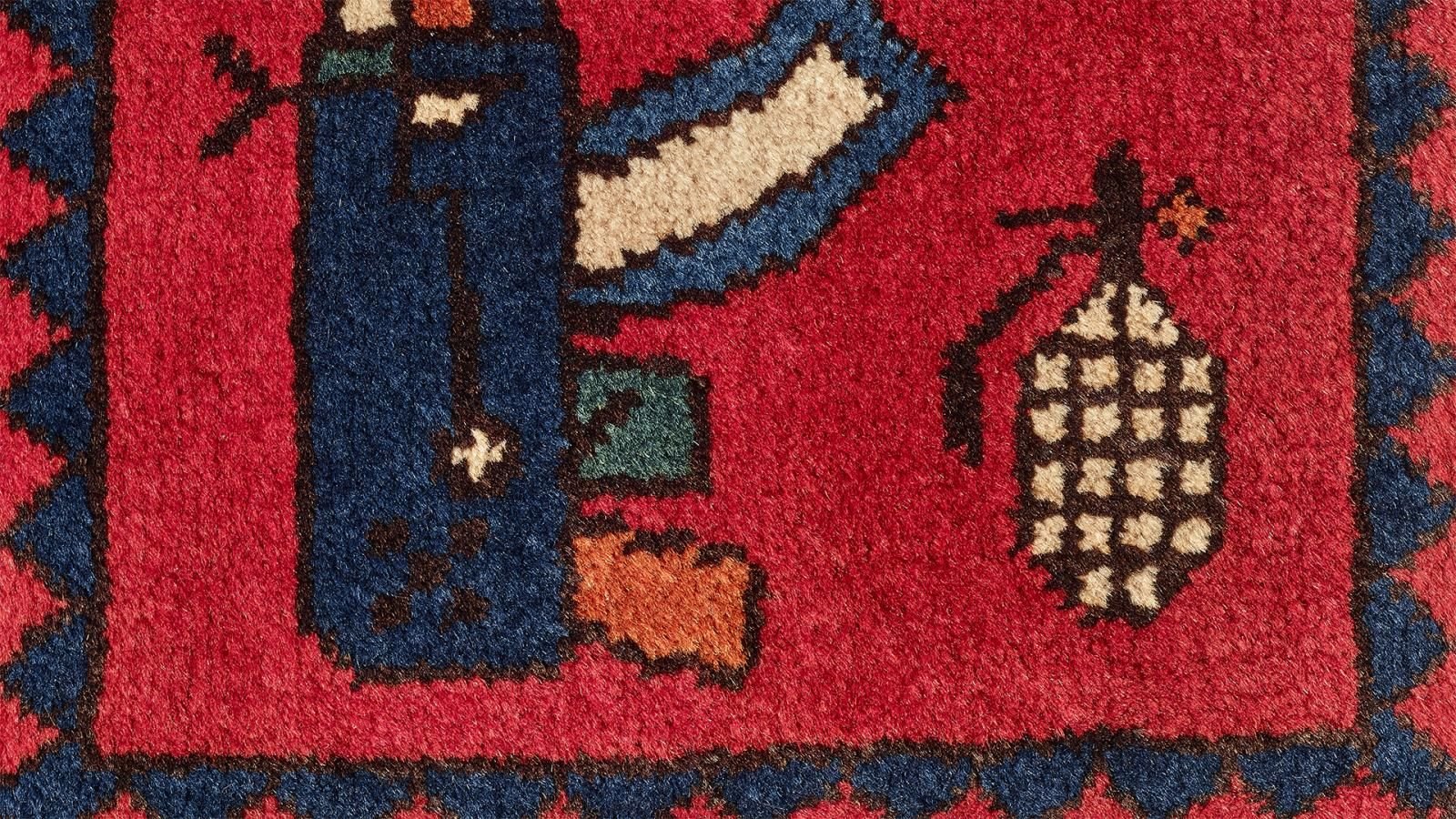 Detail of an Afghan war rug, showing a hand grenade and part of an assault rifle on a red background.
