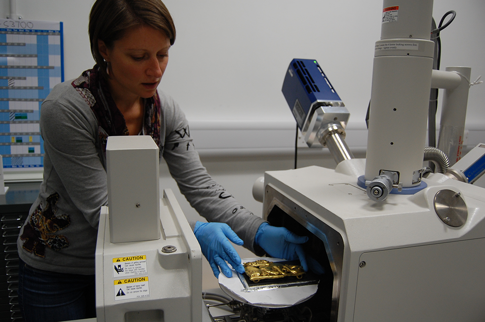 Aude Mongiatti wears blue gloves and carefully places a gold object in a machine