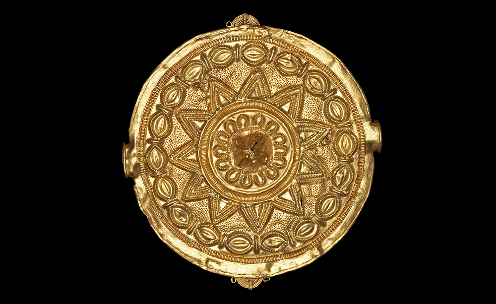 A golden disc-shaped pendant, with an ornamental design akin to the sun's rays in the centre