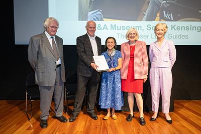 Five people standing on stage in front of a large presentation screen, two of which are holding a certificate.