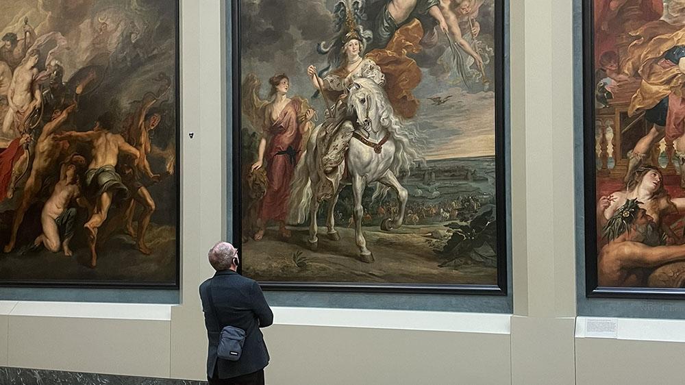 View of a Patron standing in a gallery space in front of three large-scale paintings.