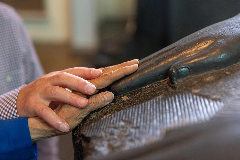 A volunteer rests their hand on the hand of a visitor who is blind or partially sighted, and helps the visitor feel the carved hand of a sculpture