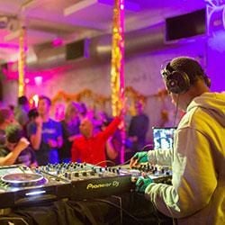 A Bubble Club DJ performing, viewed from the back, with the crowd in front dancing. The room is decorated with gold tinsel. 