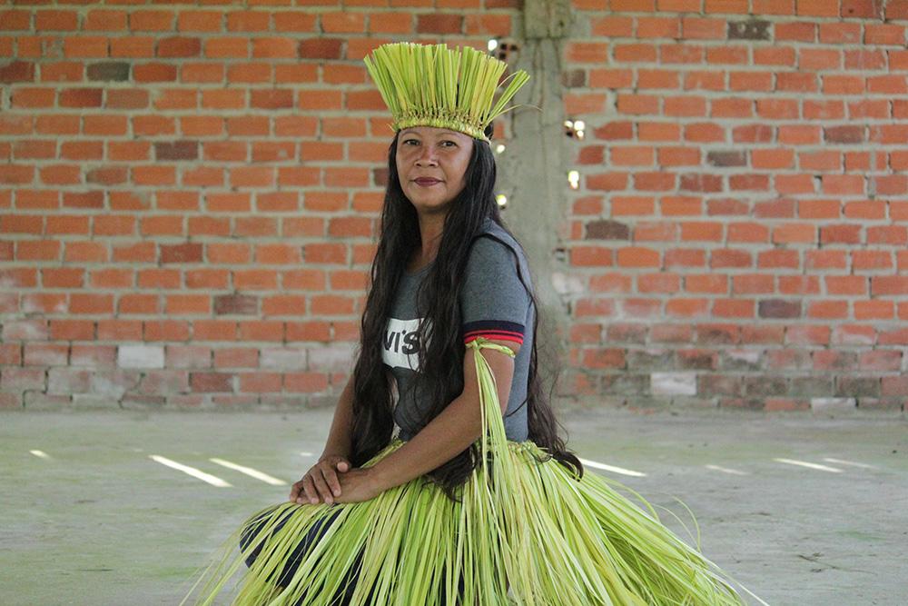 A Nawa woman wears a grey Levi's tshirt, and a bright yellow and green headdress, skirt and armbands made from plant fibre