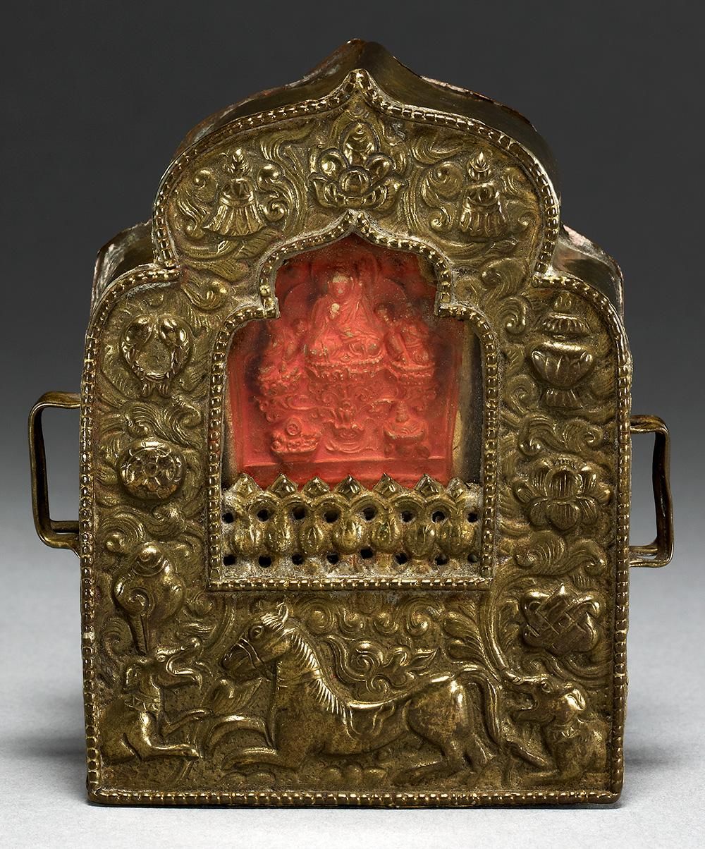 A small, intricately carved bronze case, with a red plaque visible at its centre