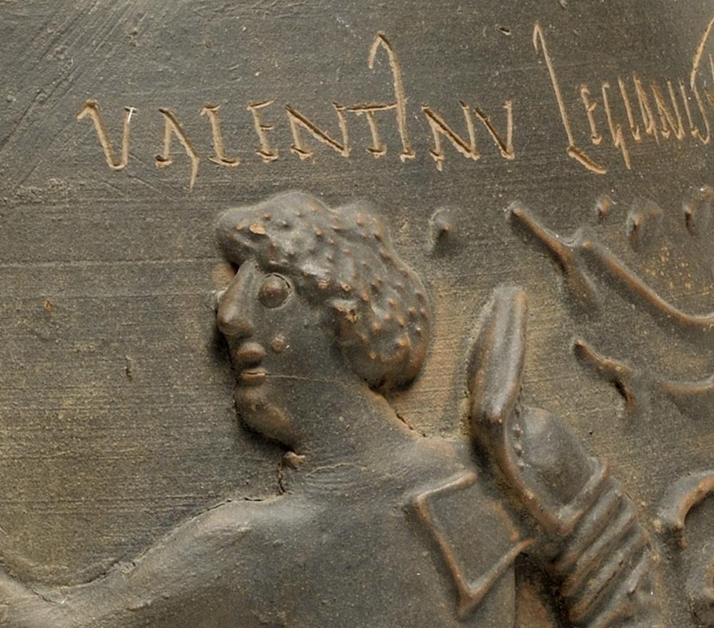 Inscription of the name Valentinus carved into the terracotta of the Colchester vase, with the face of the gladiator open-mouthed in fear below the inscription