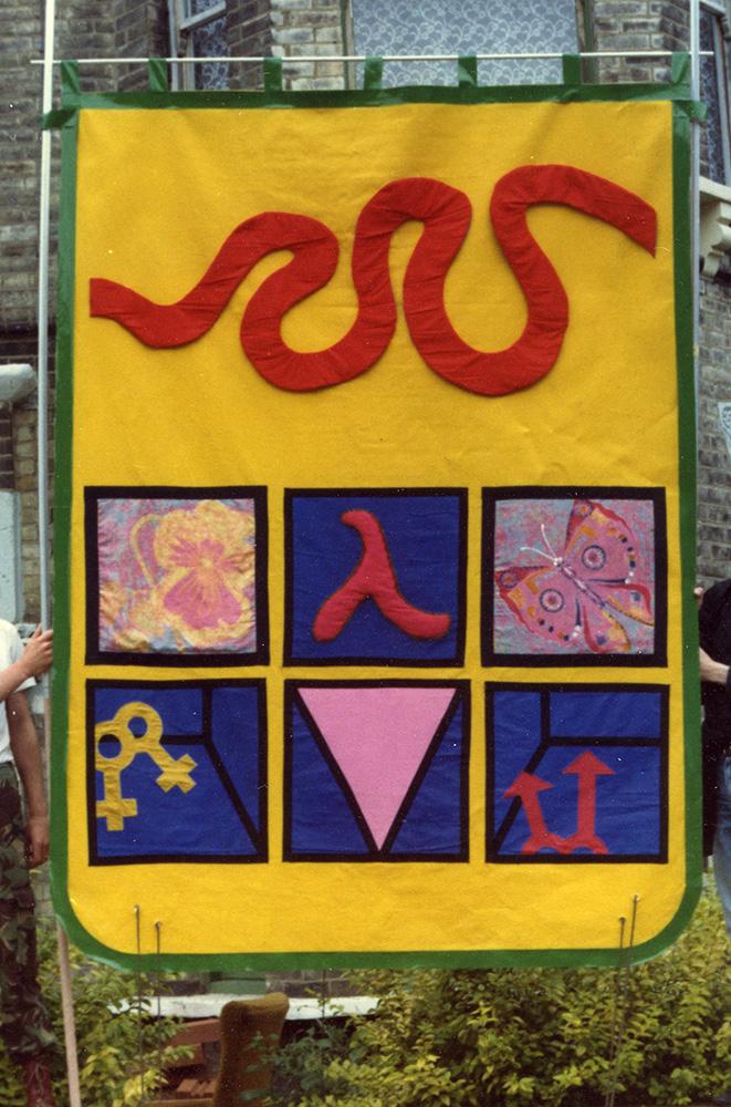 A banner with a bright yellow background and green border, with gay and lesbian symbols on it, as well as a butterfly and a flower