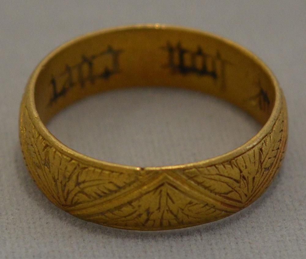 Gold ring with engraving of leaves and flowers around the outside and black engraved text inside.