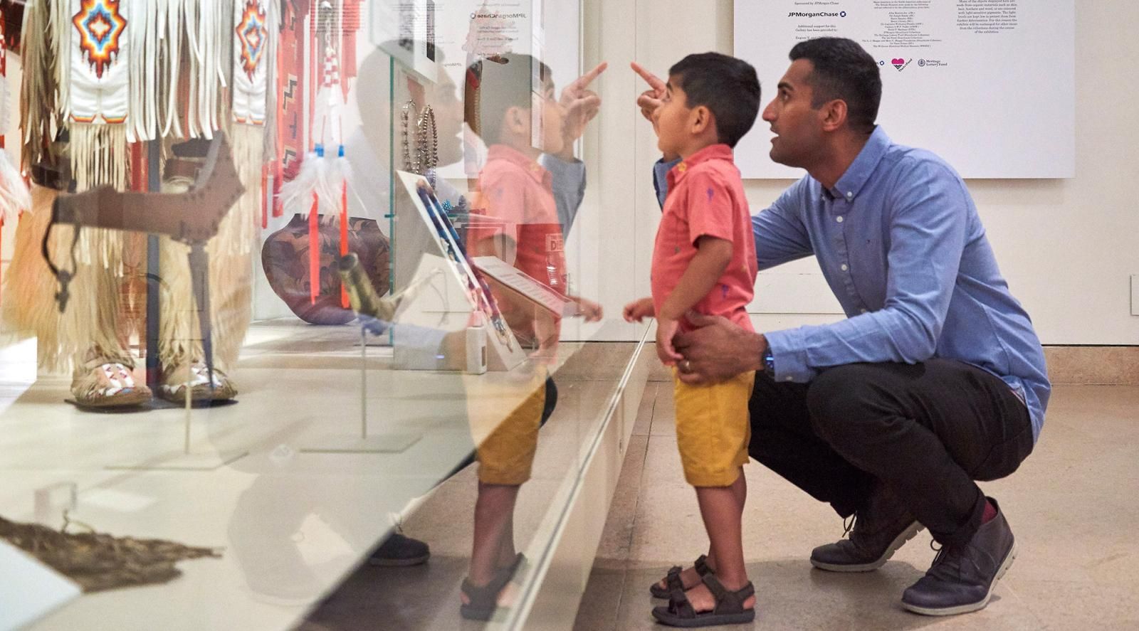 Father crouching down and pointing into display case with young son looking in