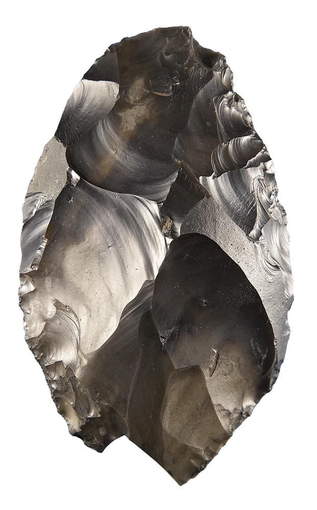 A handflint made of hard brown-grey rock that has been chipped into an oval shape with sharp points at either end