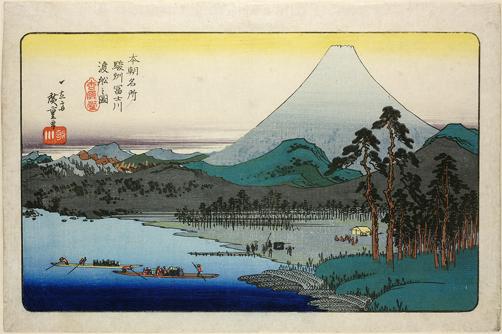 Print of Mount Fuji with a mountains behind and water in the foreground. There are boats on the water, and trees on the right bank.